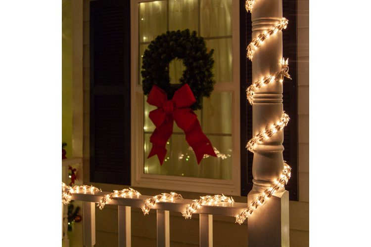 warm white Christmas string lights wrapped around a porch banister in front of a window with a festive wreath