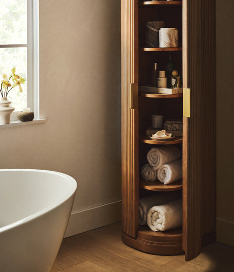 Bathroom with wood etagere cabinet stocked with towels and toiletries.