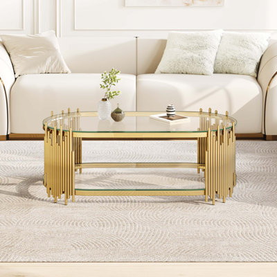 Table basse ovale à deux niveaux avec tablettes en verre trempé et base en acier inoxydable poli pour les salons modernes.