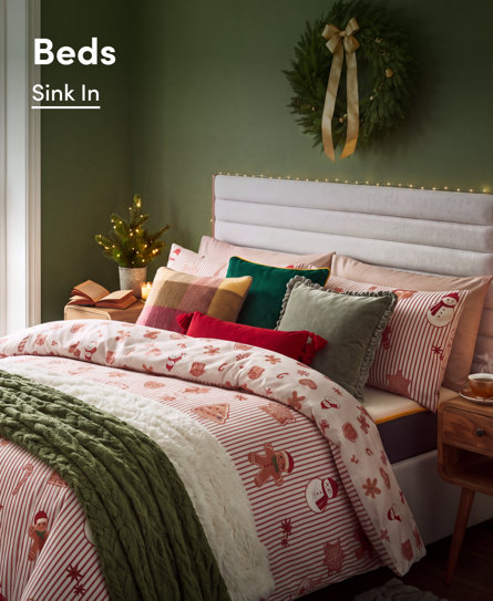 Beds, Sink In. A cosy bedroom decorated for Christmas featuring a bed with festive bedding, a green knitted throw, and a Christmas wreath on the wall.