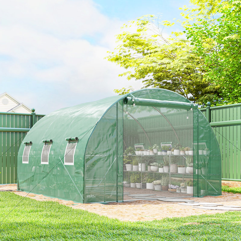 Walk-in tunnel greenhouse with a green PE cover, arched mesh door, and interior shelving filled with potted plants.
