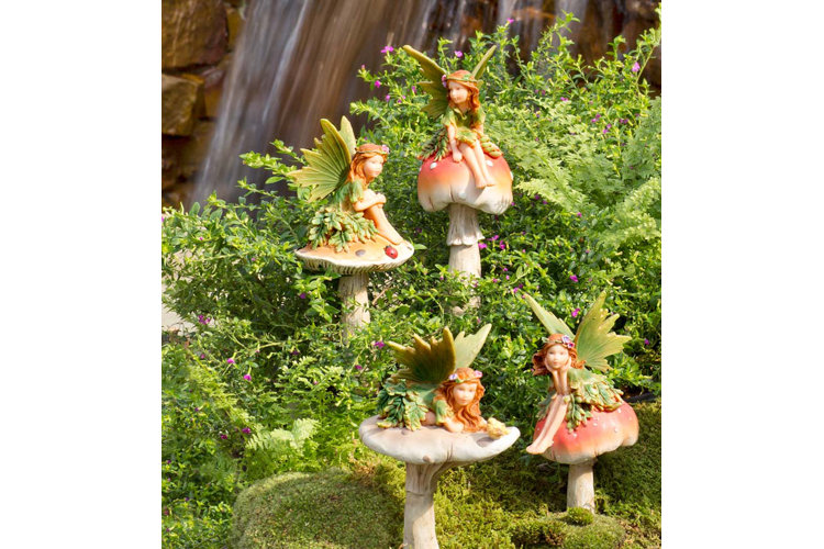 ceramic fairy figurines sitting on mushrooms in a garden