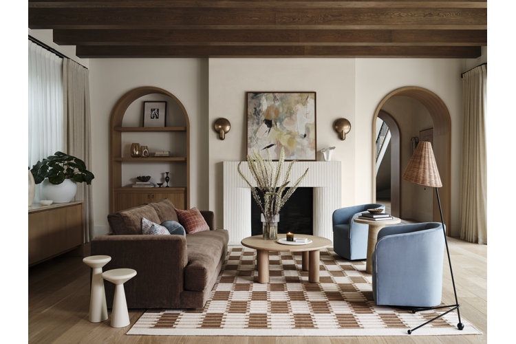 Living room with wood built in shelves and arch ivory walls and mantel brown modern sofa and light blue modern chairs on a cream and brown checkered area rug