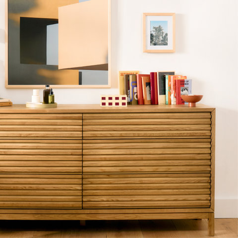 Modern oak six-drawer dresser with horizontal slatted detail, styled with books, decorative objects, and framed wall art.