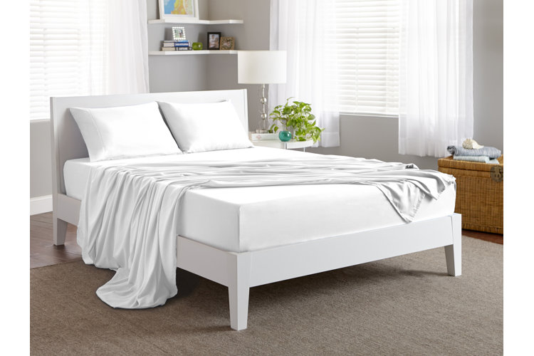 White bed with white fitted sheet and white top sheet draped across it