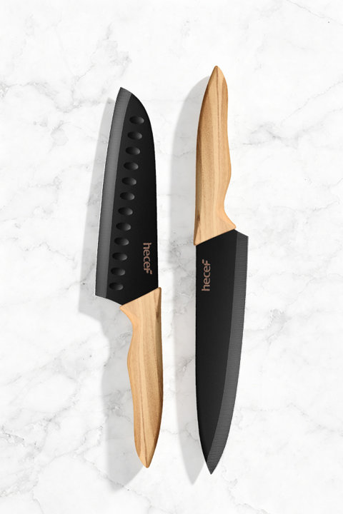 Two Hecef kitchen knives with black blades and light wood handles placed on a white marble surface.
