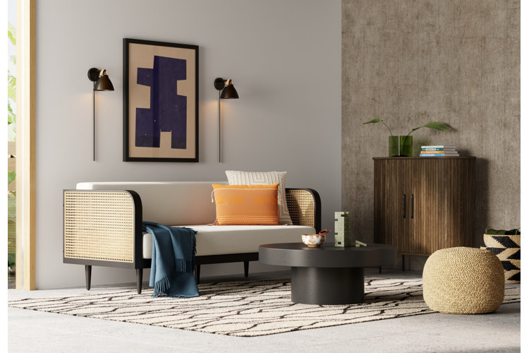 Daybed being used as a sofa in a modern living room with a black pedestal coffee table and abstract art.