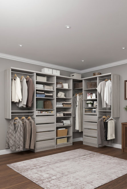L-shaped light wood reach-in closet organization system featuring hanging rods, open shelving, and drawers on a gray wall with wood flooring.