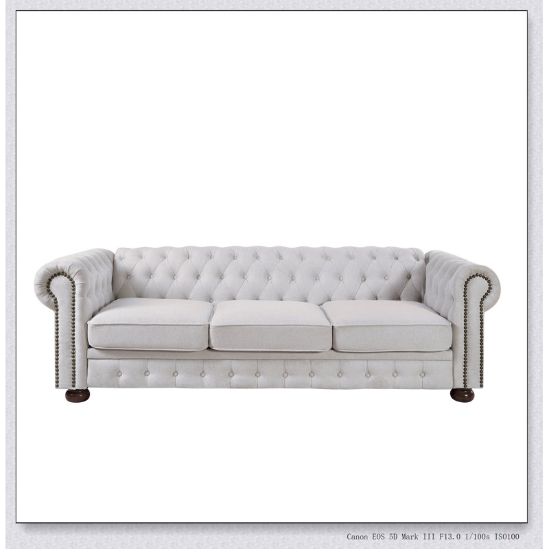 Canapé Chesterfield en tissu de lin beige avec un design classique et des sièges confortables, parfait pour les salons élégants