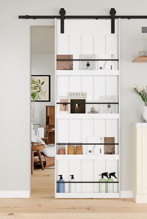 White barn door featuring built-in display shelves with magazines, small jars, and cleaning bottles, mounted on a black sliding rail system.