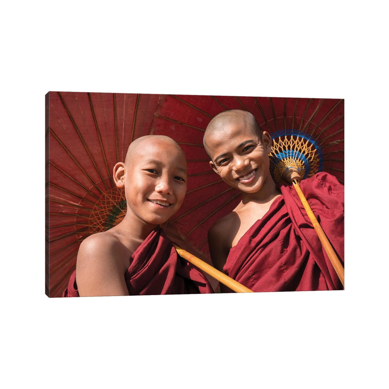 Two Young Buddhist Monks Smiling And Holding Red Umbrellas, Myanmar by Jan Becke - Wrapped Canvas Print