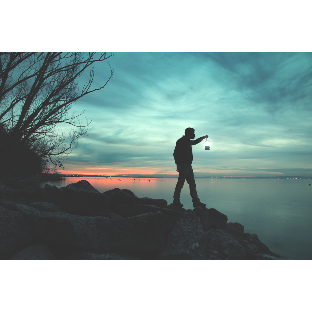 Leinwandbild Mann mit Fackel geht auf Felsen am See in der Nacht von Francescoch