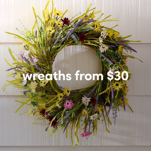 A colorful outdoor summer wreath featuring yellow, pink, and purple wildflowers hanging on white siding from $30.