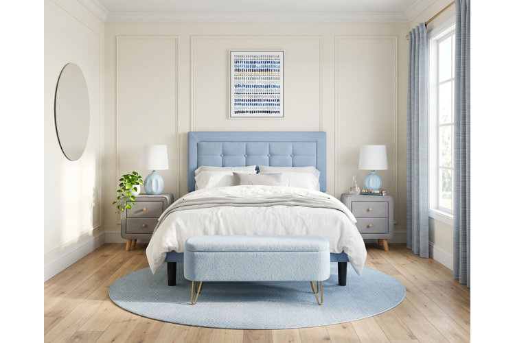 transitional-style bedroom with a French blue upholstered bed frame and matching bench with a pale blue area rug and table lamps
