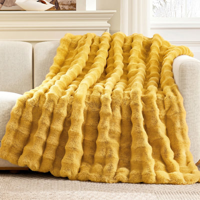 Yellow faux fur throw blanket with a textured bubble wave pattern draped over a beige sofa.