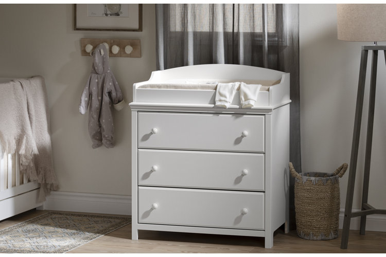 nursery with a white changing table dresser in front of light gray curtains
