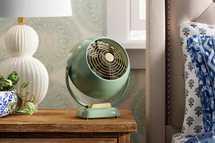 mint green tabletop fan on a wood nightstand next to a white ceramic lamp and a blue floral planter