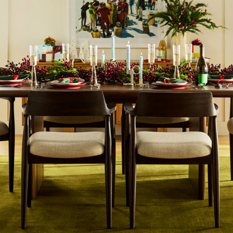 Modern dining room with a light wood table, dark wood chairs, a gold three-light pendant, and a checkered area rug in front of a window with autumn trees.