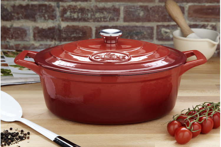 what is a dutch oven, red dutch oven on a wood countertop with tomatoes on a vine