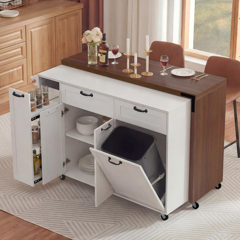 Un grand îlot de cuisine blanc avec une table de salle à manger rétractable, une armoire de rangement pour poubelle et un support à épices escamotable; Il est également équipé de roulettes pour faciliter le déplacement.