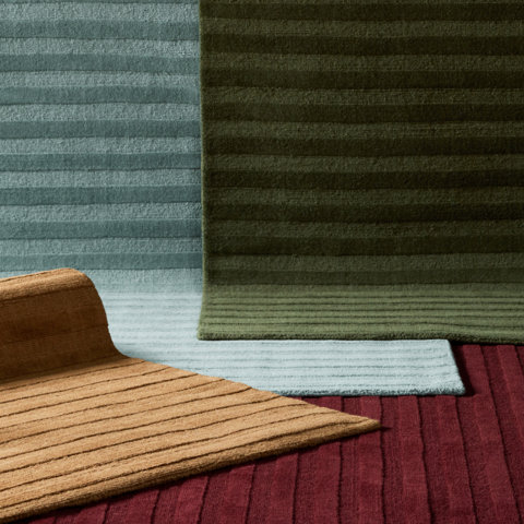 Close-up of overlapping area rugs featuring a variety of textured, geometric block patterns in shades of brown, olive green, and neutral beige.