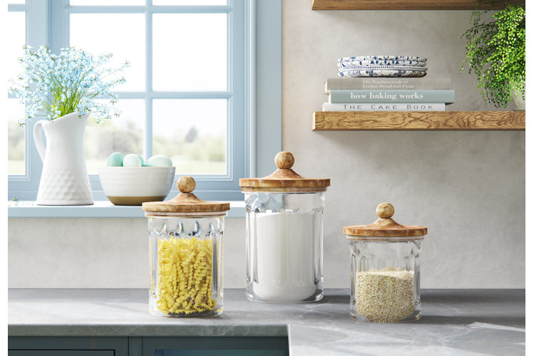 three glass canisters in front of a windowsill with a vase of blue flowers