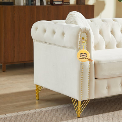 Canapé Chesterfield en velours avec deux coussins ronds, orné de clous en cuivre et de boutons capitonnés, et reposant sur des pieds en métal. Un système d'accroche permet de suspendre des décorations décoratives.