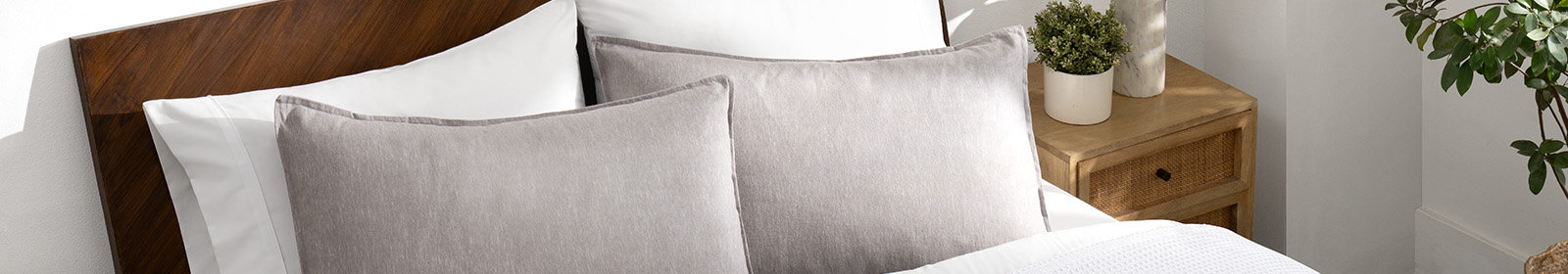 A view of the head of a bed with two pillows covered by light grey pillow shams