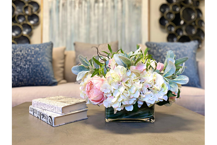 hydrangeas arranged with greenery in a glass vase sitting on a coffee table