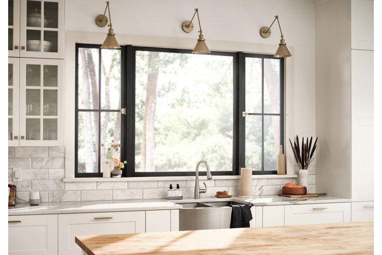 sink in a white kitchen with three gold armed wall sconces above. black window over sink and white and glass dish cabinets on either side