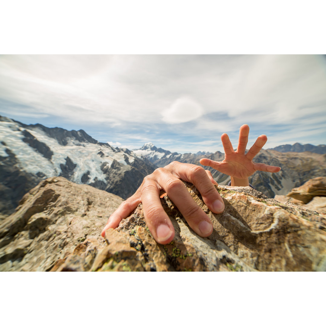 Menschliche Hände greifen nach dem letzten Felsen auf dem Berggipfel von Swissmediavision - Kunstdrucke