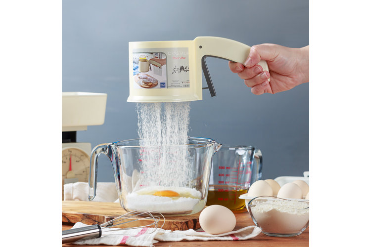 person holding flour sieve over a bowl of eggs