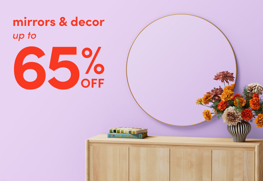 Mirrors and decor up to 65% off featuring a round gold mirror hanging above a light wood console table with flowers and books.