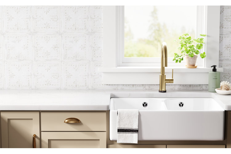 closeup of a white kitchen sink with a white tile backsplash and light beige cabinets