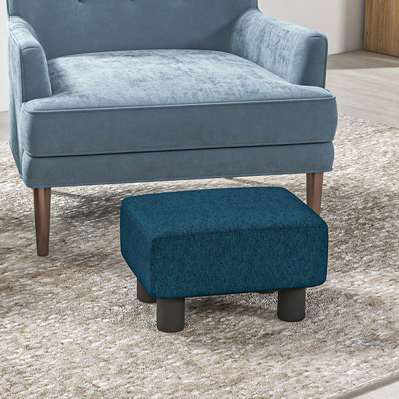 Le tabouret Blue Cube, en lin recouvert de solides pieds en plastique, ajoute du confort au repose-pieds en tissu bleu, créant une ambiance relaxante