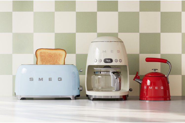 Retro-inspired countertop with pastel SMEG toaster, coffee maker, and red kettle against green checkerboard tile backsplash.