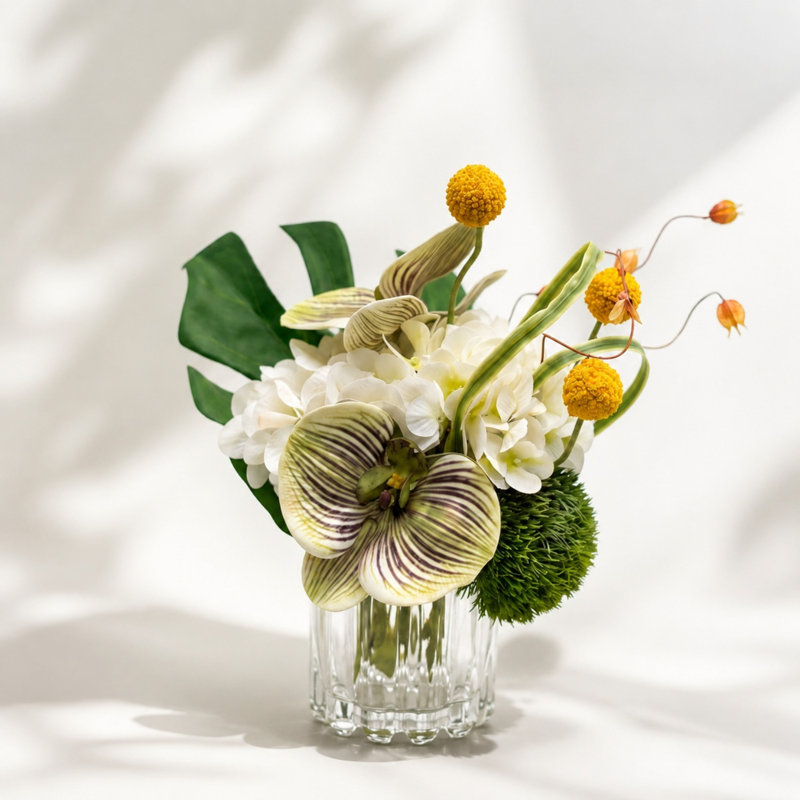 Arrangement artificiel orchidée et boule de Billy avec hortensia dans un vase en verre nervuré