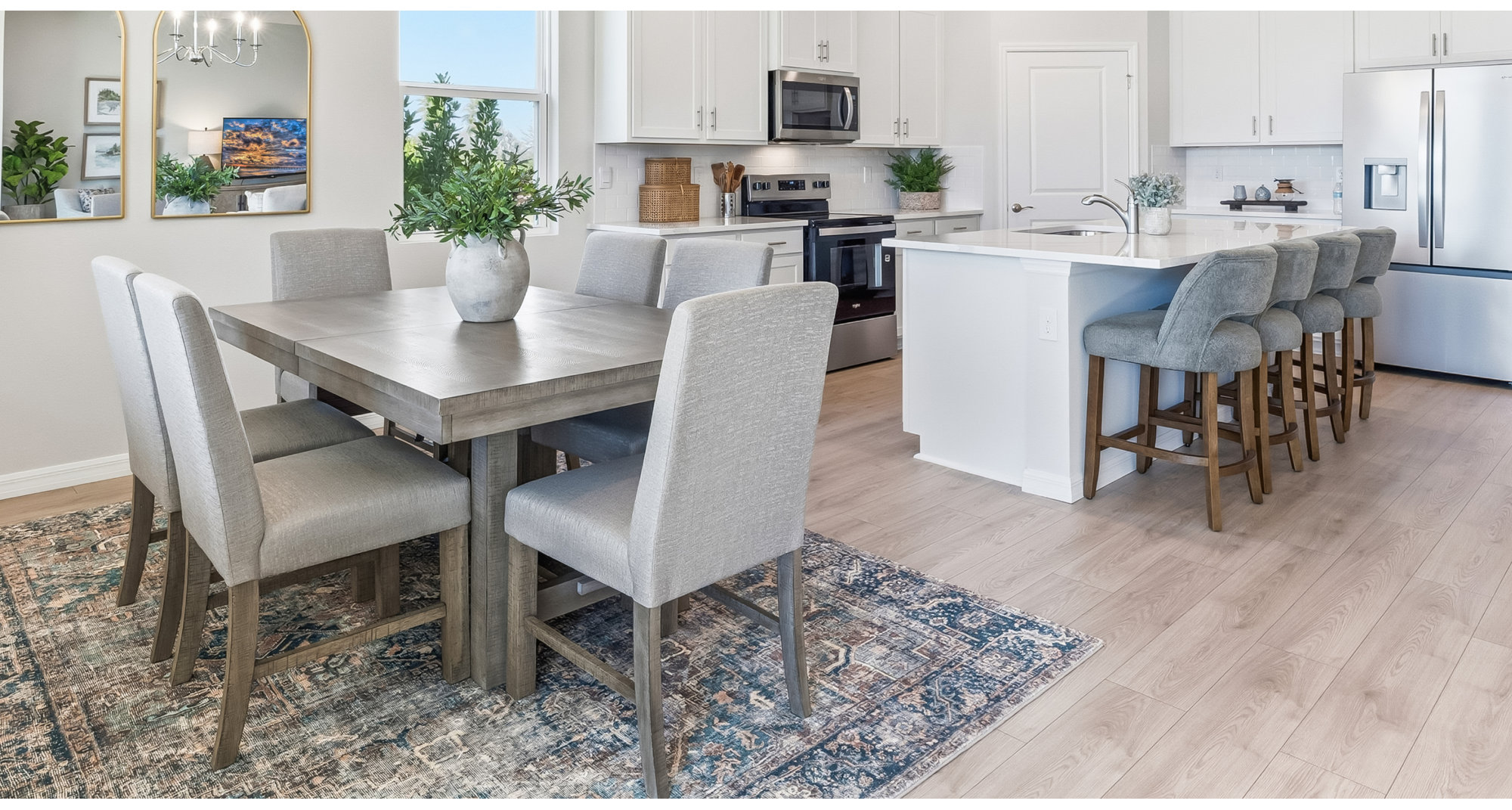 Dining room with a wood table and gray chairs, adjacent to a kitchen with a white island.