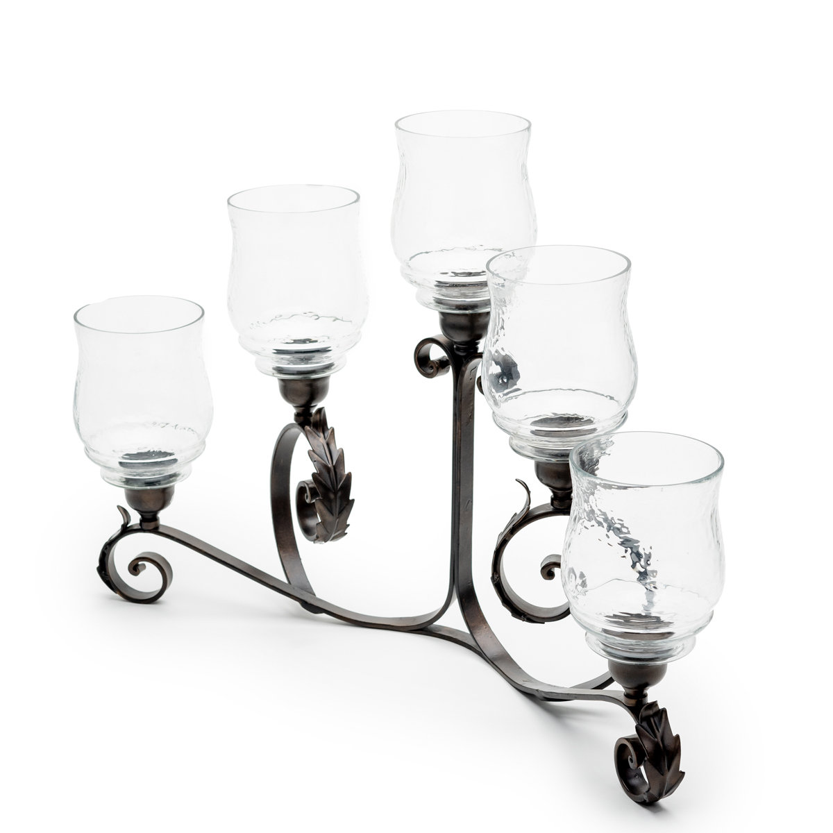 Angled view of a five-arm wrought iron candle holder with clear glass hurricane shades, ornate scrollwork, and decorative leaf accents.