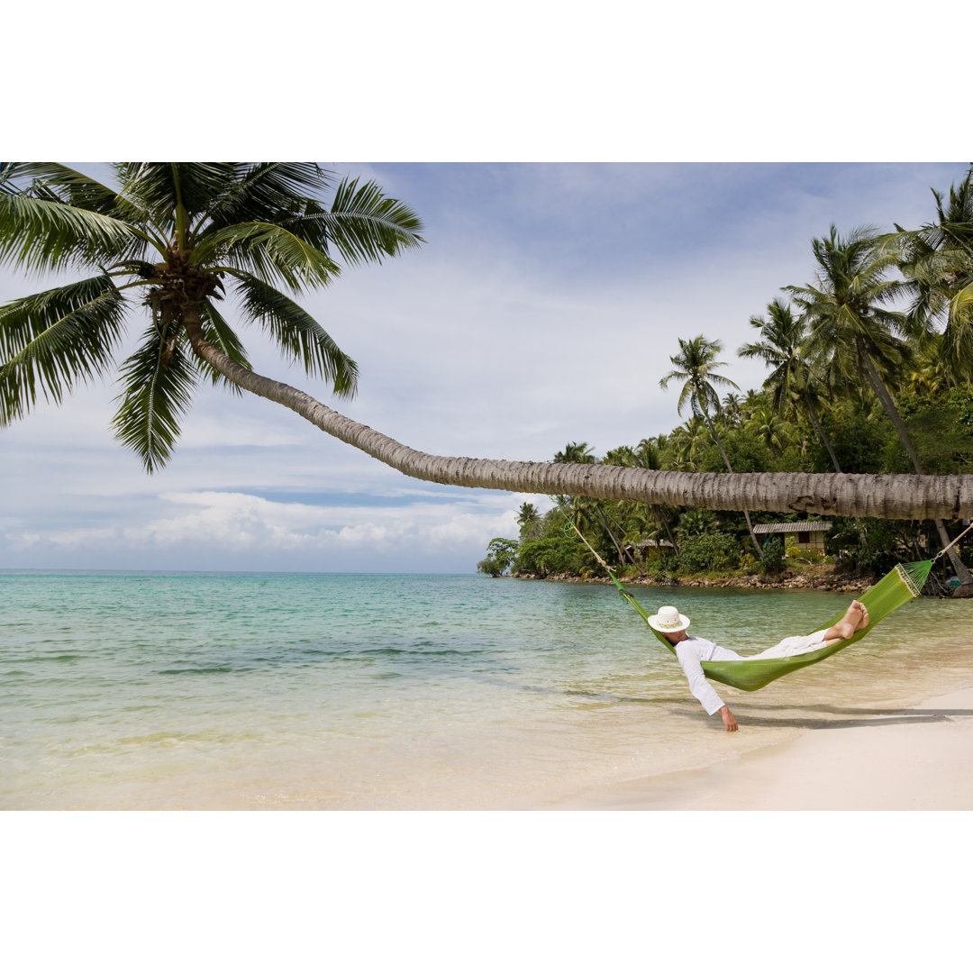 Mann liegt in einer grünen Hängematte am Strand und hängt an einer Palme