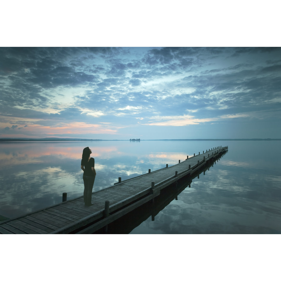 Silhouette einer jungen Frau, die in der Abenddämmerung auf einem Steg am See steht