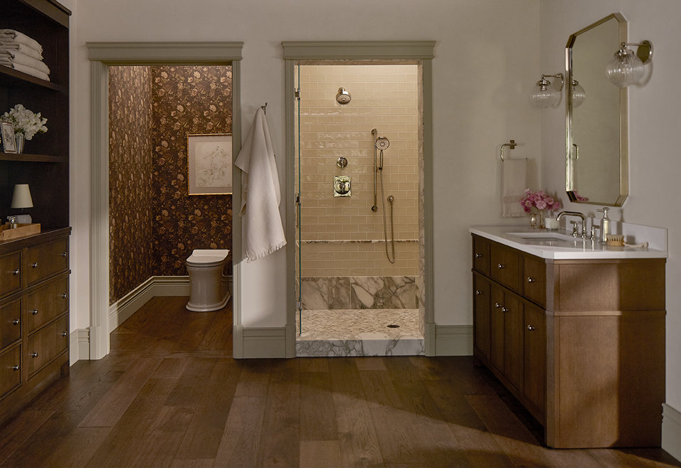 Traditional bathroom with dark wood cabinets, a marble-floored walk-in shower with beige subway tile, and a separate water closet featuring floral wallpaper.
