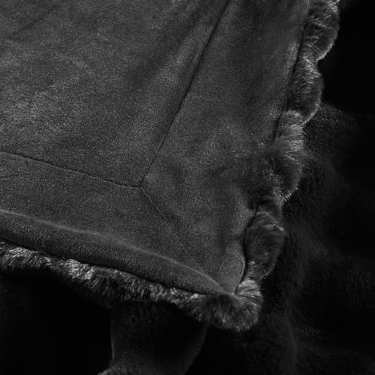 Close-up of a black faux fur throw blanket showing soft textured surface, plush trim, and stitched corner detail