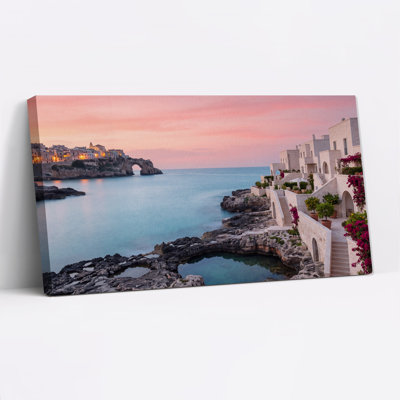 Tableau sur toile représentant une ville côtière avec des bâtiments blancs et une arche rocheuse au coucher du soleil