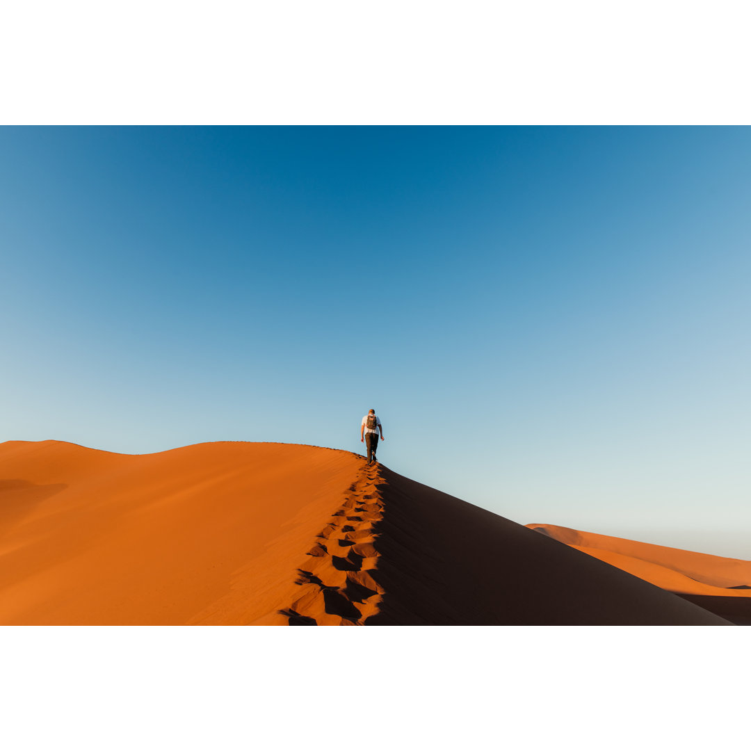 Mann Reisender genießt den malerischen Sonnenaufgang vom Gipfel der Düne in Sossusvlei, Namibia von Anastasiia Shavshyna...