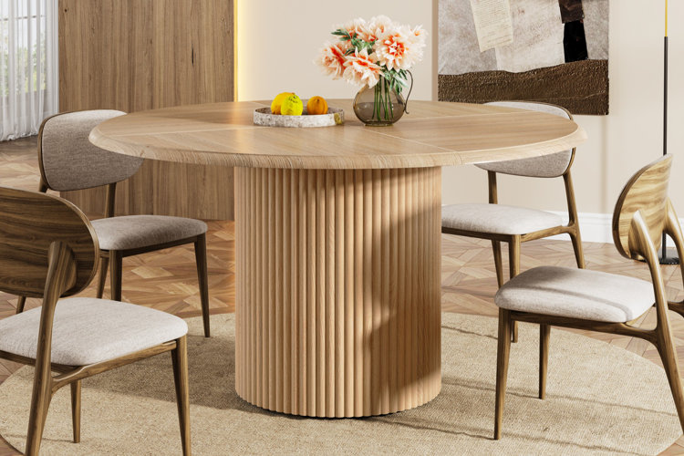 round wooden dining table with fluted pedestal base, four cushioned chairs, and vase of flowers