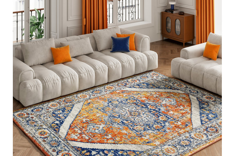living room with a large white sofa with orange and yellow throw pillows. large area rug with blue and orange tones