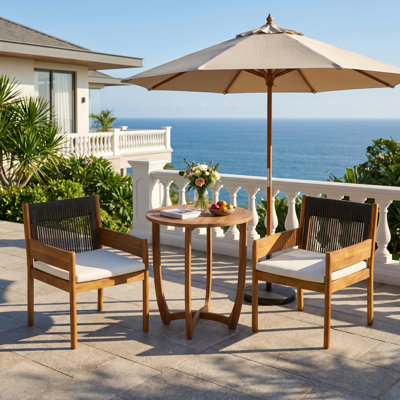 Ensemble bistro de patio Celia pour 2 personnes, style côtier moderne, en bois d'acacia, avec fauteuils à accoudoirs tressés, coussins et table ronde à lattes.