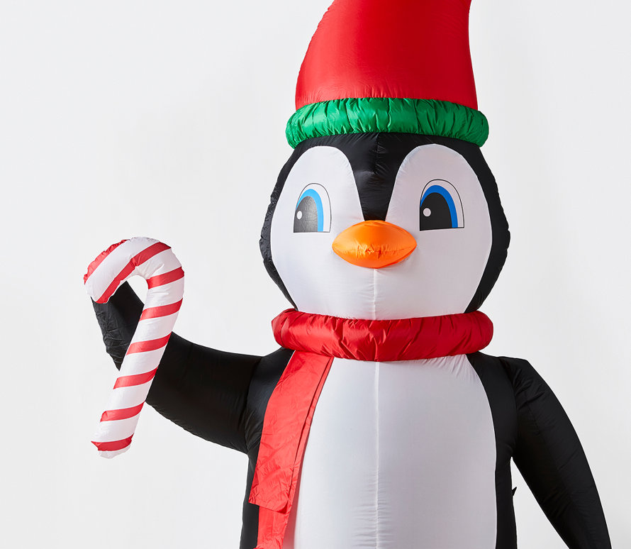 Pingouin gonflable portant un chapeau et une écharpe rouges, et tenant une canne en sucre.