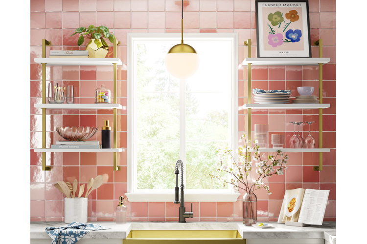 Pink kitchen backsplash behind a gold apron sink with a tiered white and gold shelf on either side. Gold pendant light hanging down